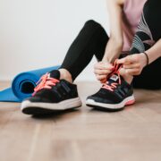 anonymous slender female athlete tying shoelaces near sport accessories