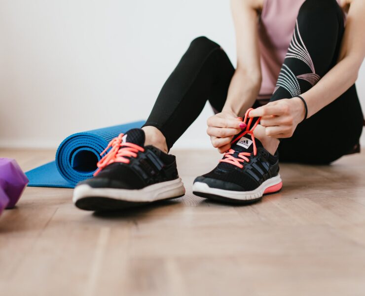 anonymous slender female athlete tying shoelaces near sport accessories