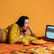 woman in yellow long sleeve shirt watching tv and eatinghi