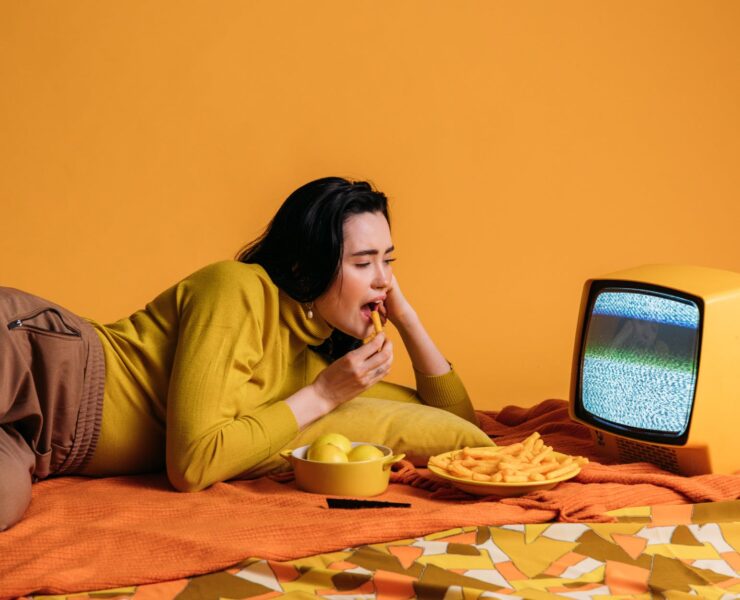 woman in yellow long sleeve shirt watching tv and eatinghi