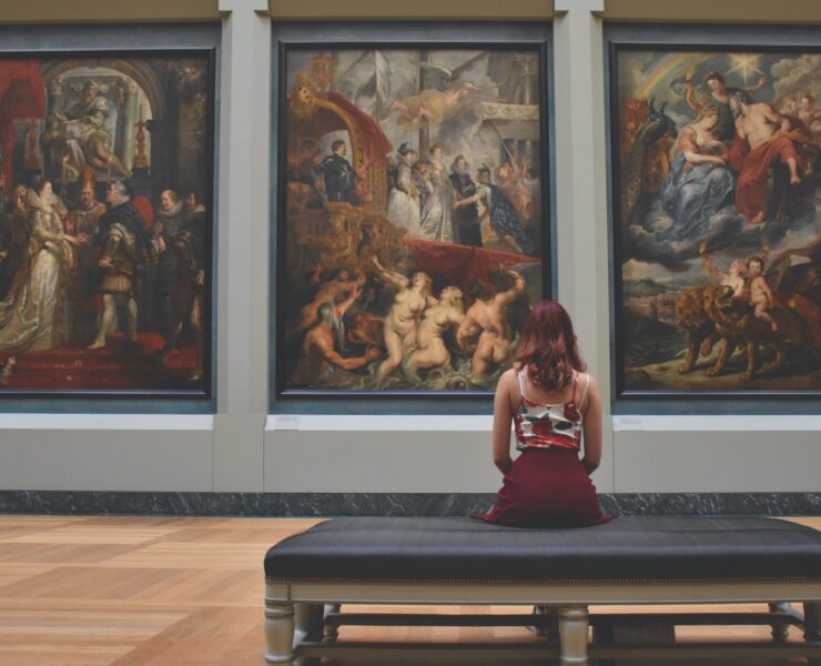 woman sitting on ottoman in front of three paintings